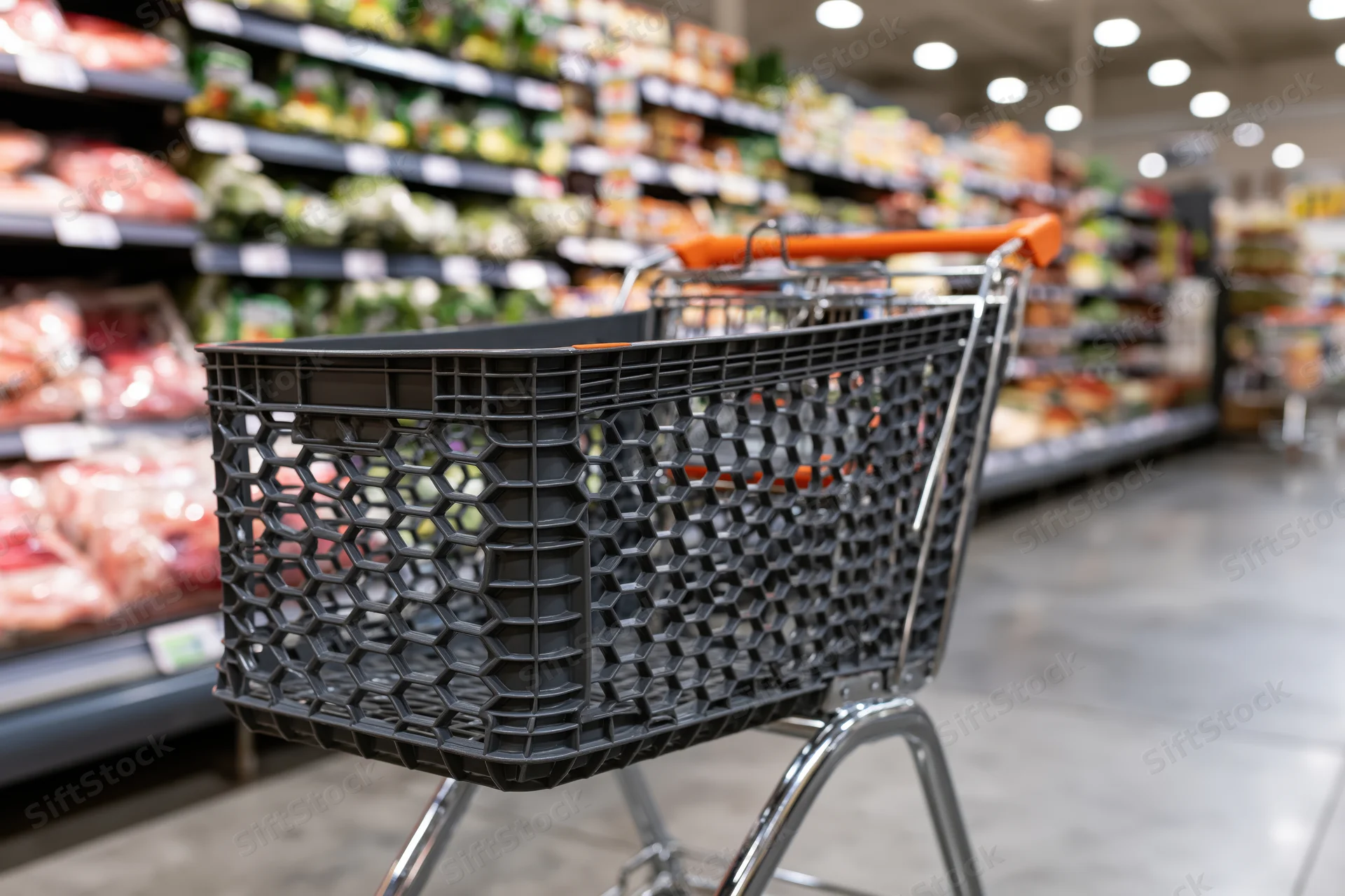 Empty dark grey plastic shopping cart with orange handle in a supermarket aisle lined with refrigerated food shelves