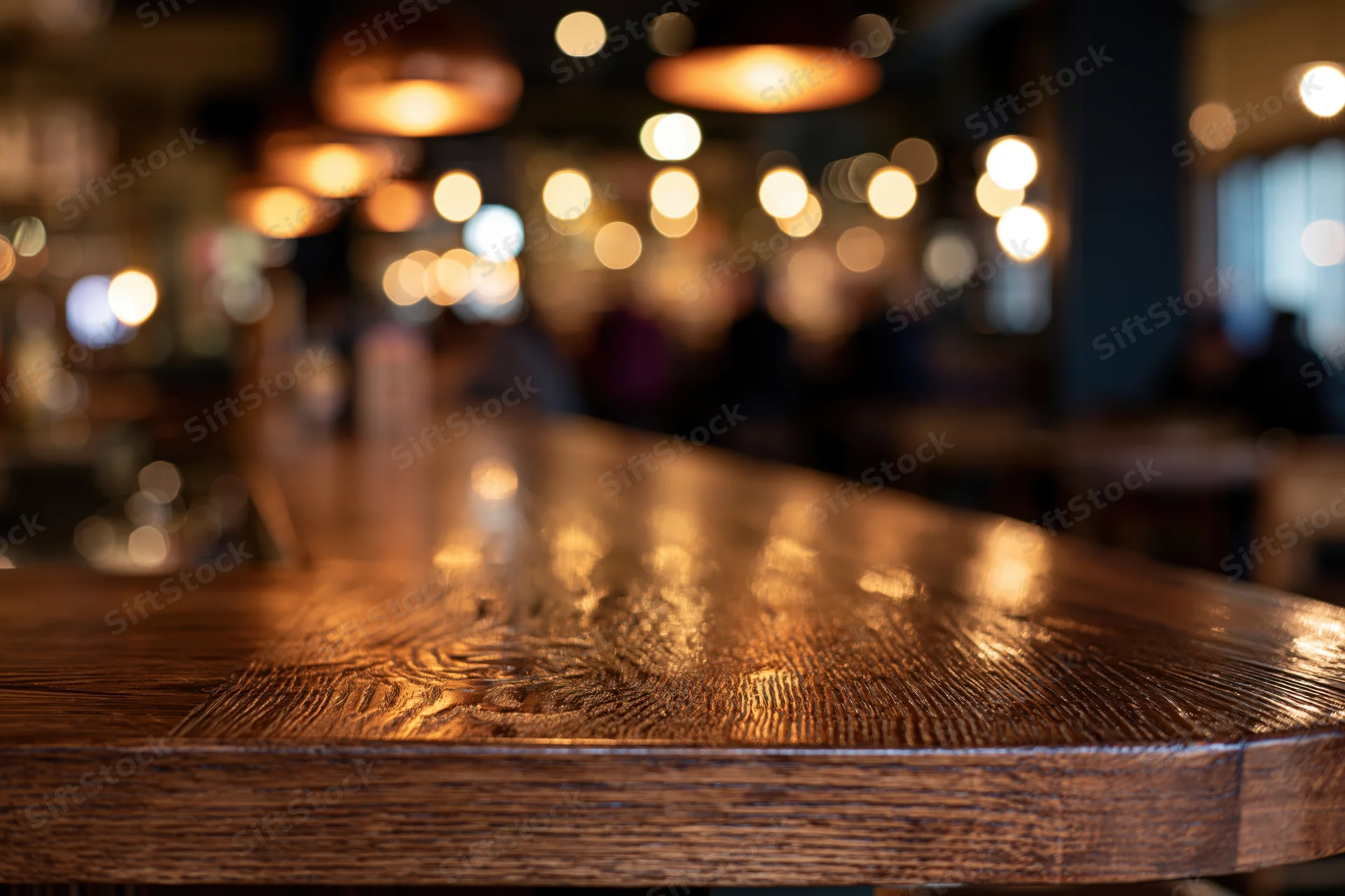 Wooden bar counter in sharp focus with blurred restaurant interior and warm lights in background