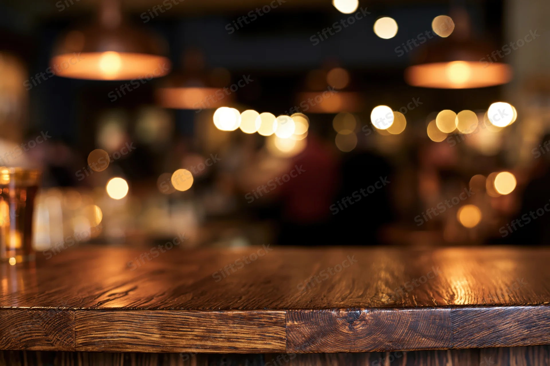 Dark wooden bar counter in sharp focus with blurred restaurant interior and warm pendant lights in background