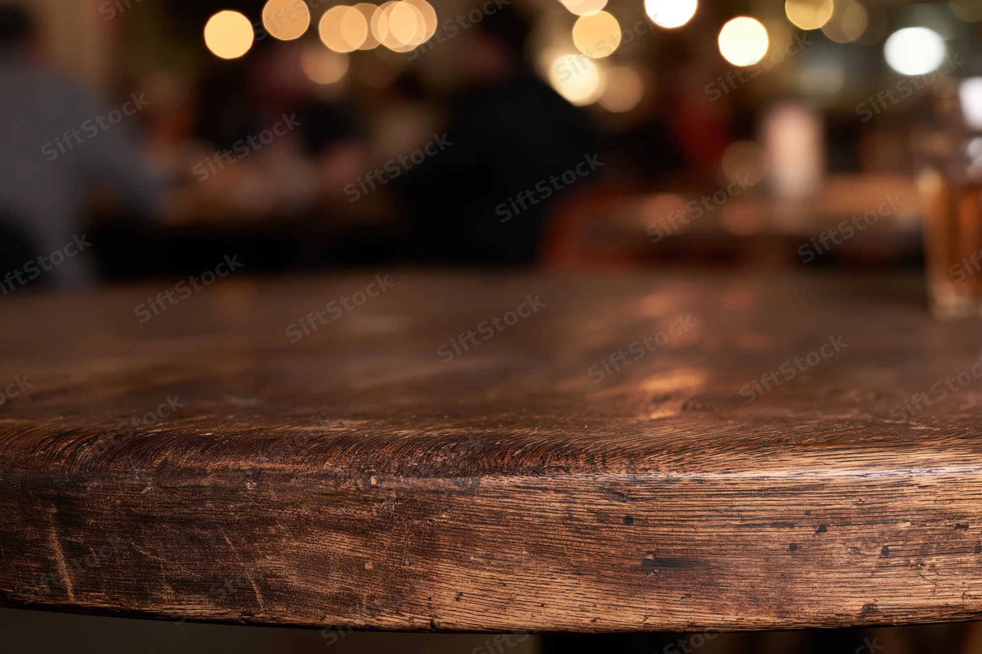 Closeup of dark wooden table surface in restaurant with blurred background of people and warm lights