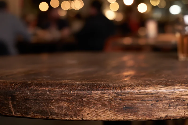 Closeup of dark wooden table surface in restaurant with blurred background of people and warm lights