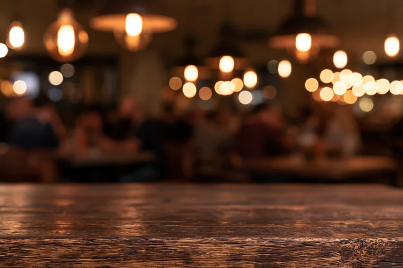 Dark wooden table in focus with blurred restaurant interior and warm lights in background