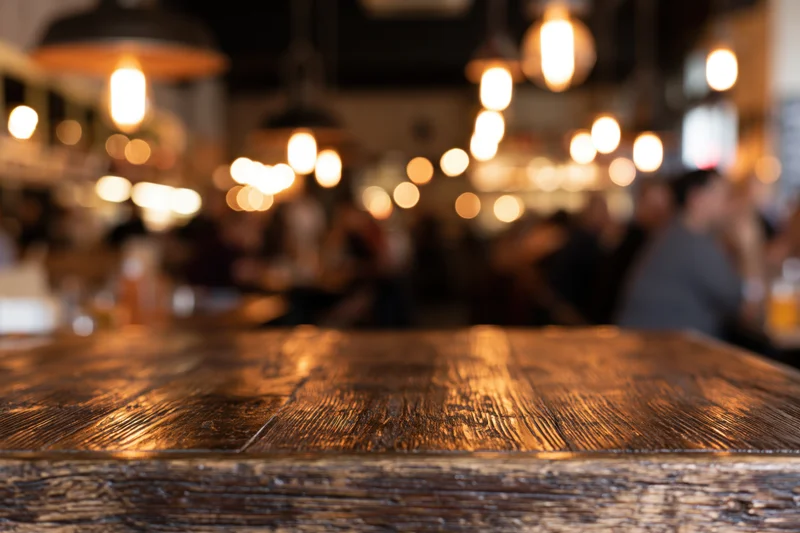 Dark wooden table in focus with blurred restaurant interior and warm lights in background