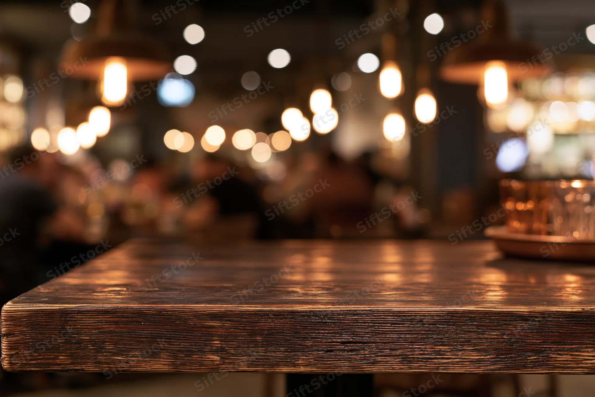 Dark wooden table in foreground with blurred restaurant interior and warm pendant lights behind