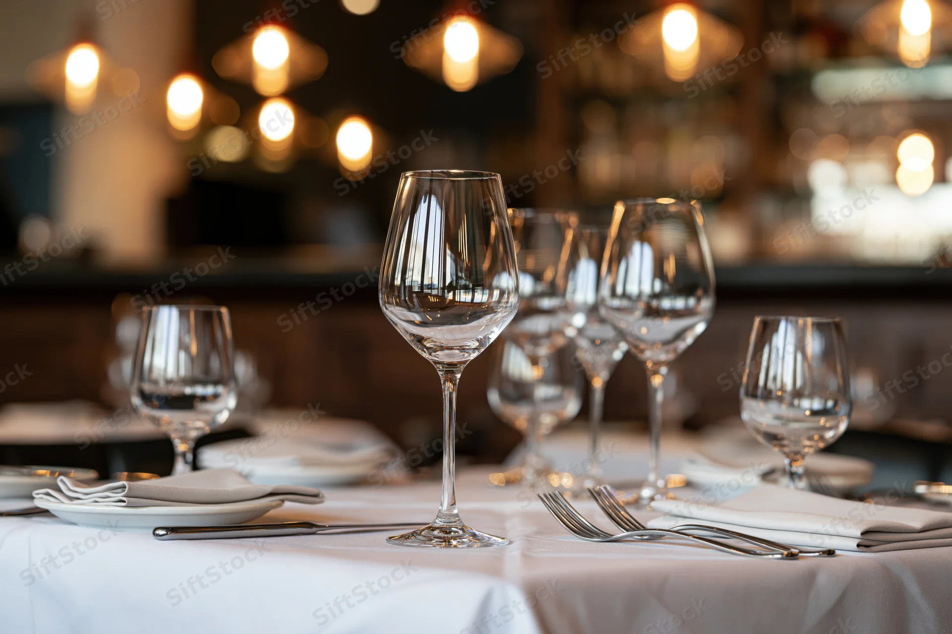 Fine dining table set with wine glasses and silverware on white cloth in restaurant interior