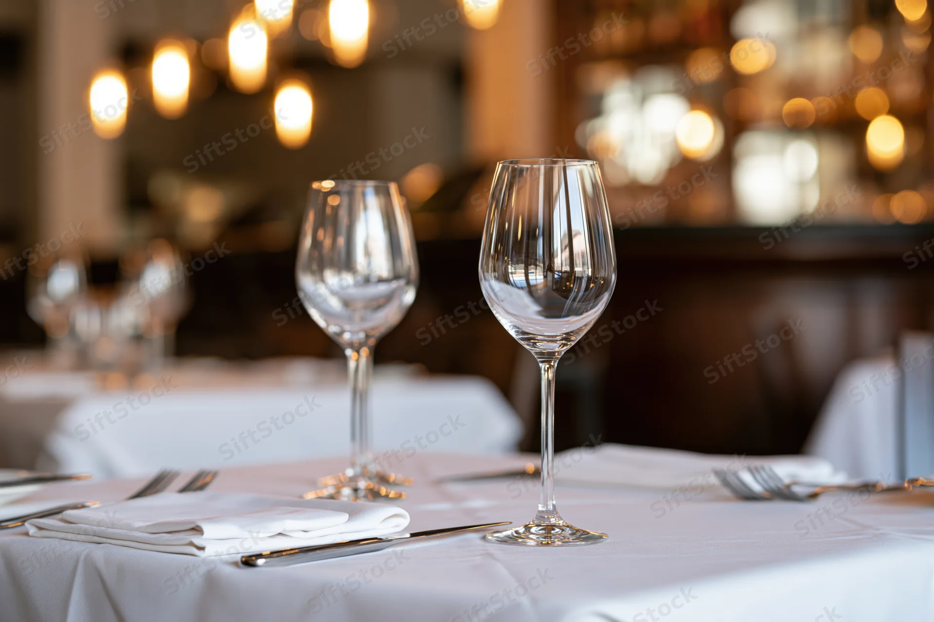 Fine dining table set with wine glasses and cutlery on white linen in a restaurant interior