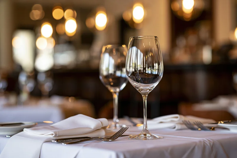 Fine dining table set with wine glasses and cutlery on white cloth in restaurant interior