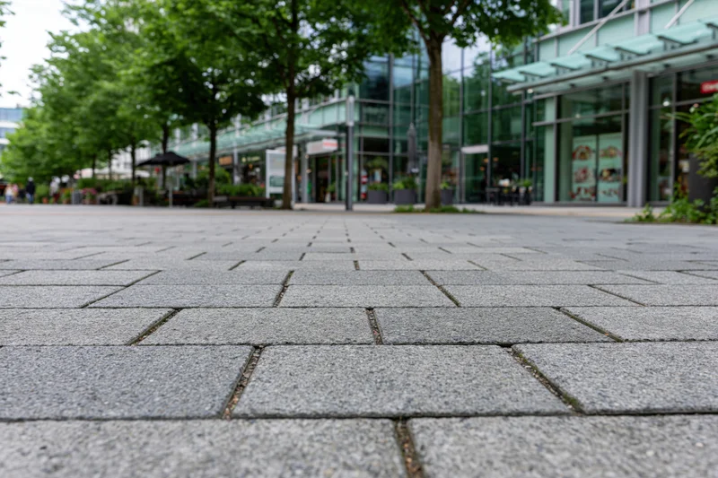 Low-angle view of gray stone pavement leading to modern glass storefronts in an urban plaza
