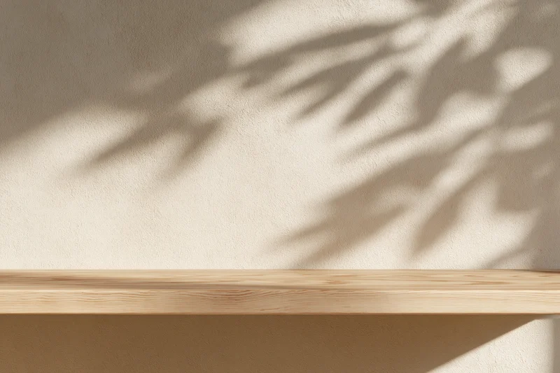 Light wood shelf mounted on textured plaster wall with dappled leaf shadows