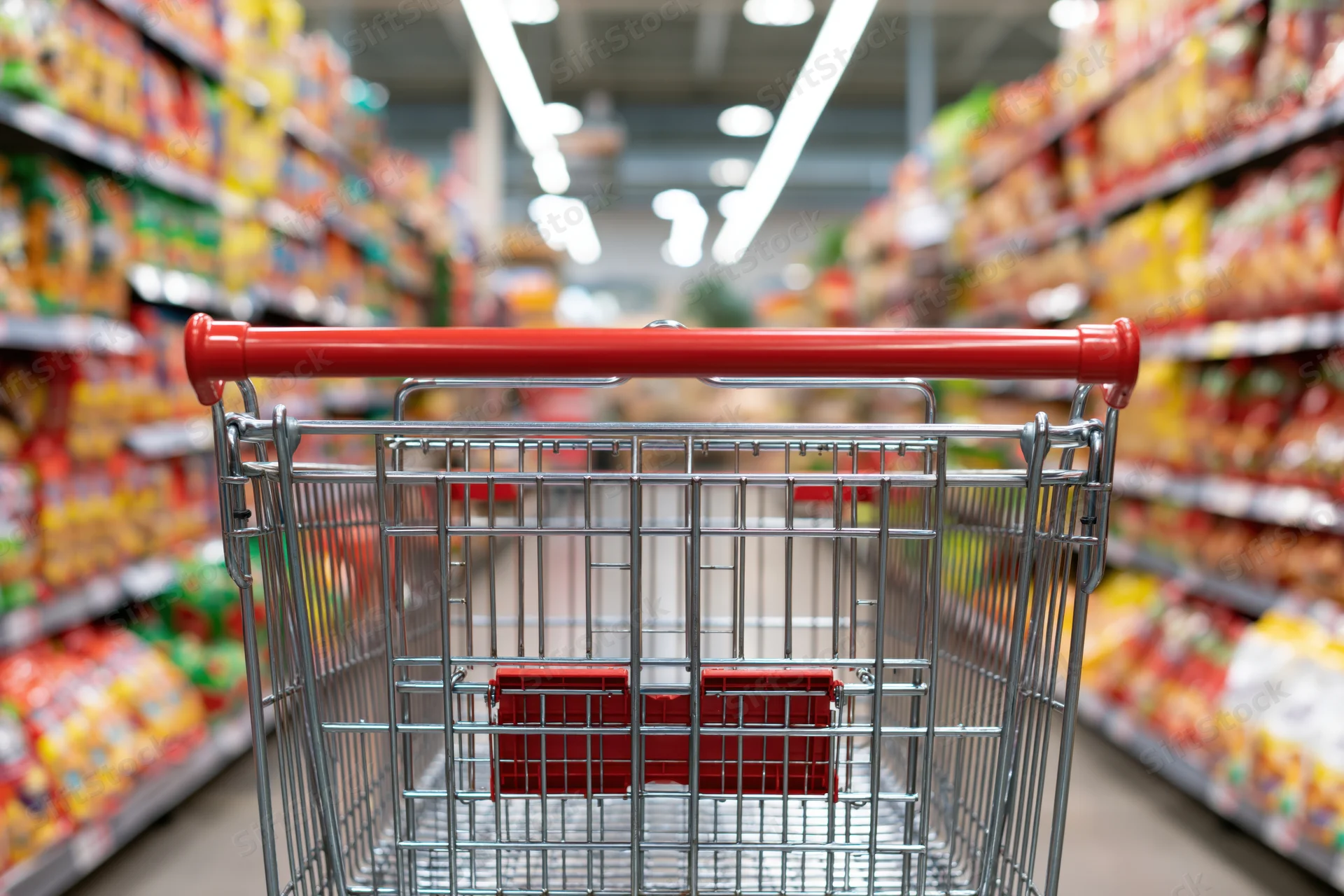 Empty metal shopping cart with red plastic child seat viewed down supermarket aisle