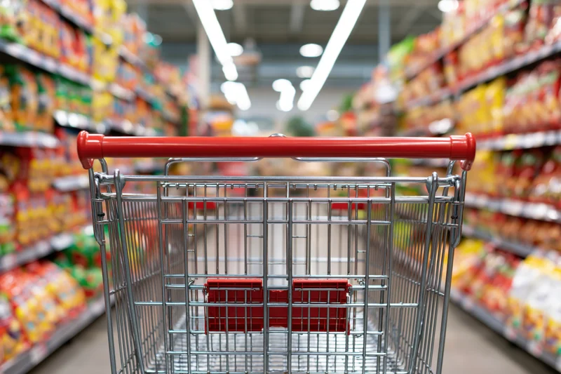 Empty metal shopping cart with red plastic child seat viewed down supermarket aisle