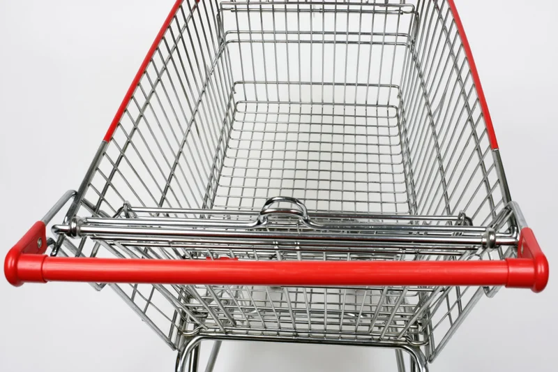 Empty metal shopping cart viewed from above with red handle against white background