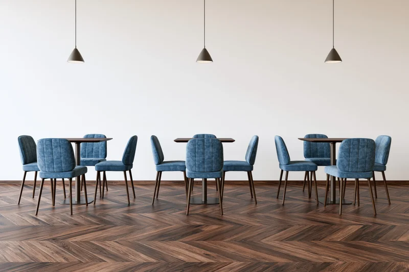 Modern cafe interior with small square tables and blue upholstered chairs arranged on herringbone wood flooring