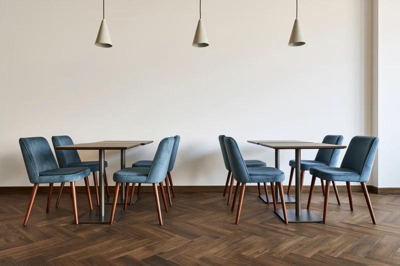 Modern cafe interior with square tables and blue chairs arranged on herringbone wood flooring