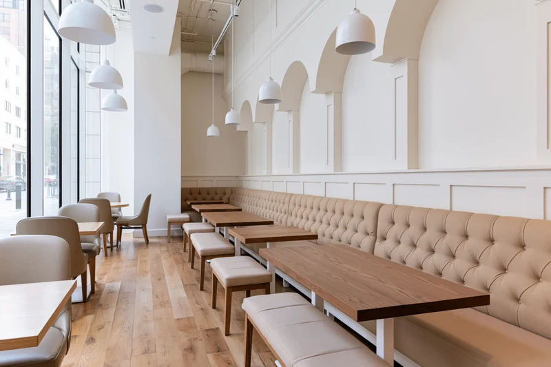 Modern cafe interior with wooden tables and tufted benches along arched walls