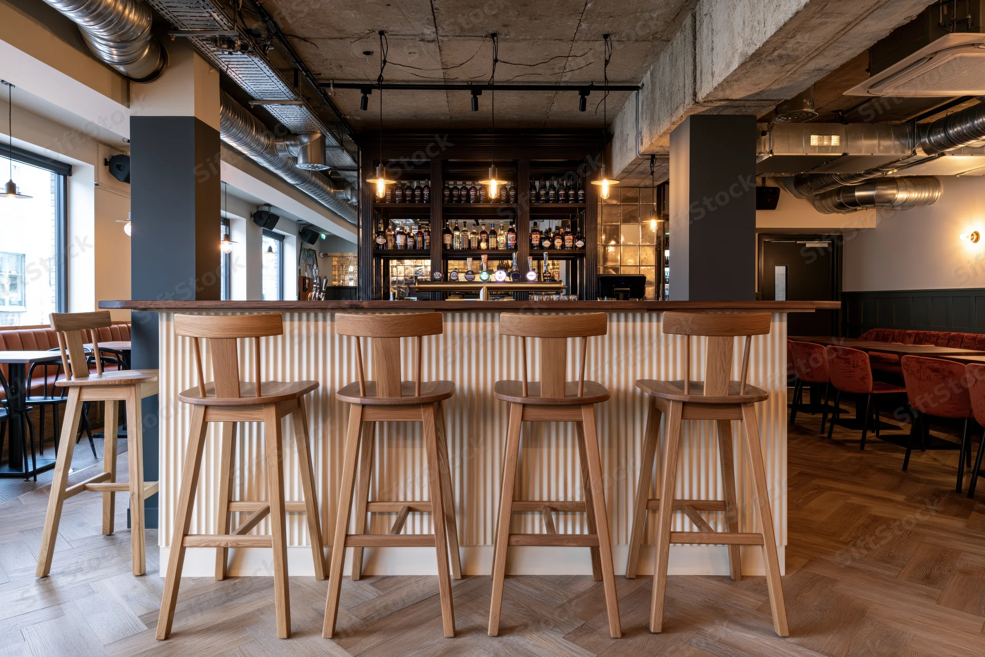 Modern gastropub interior with wooden bar stools and exposed industrial ceiling features