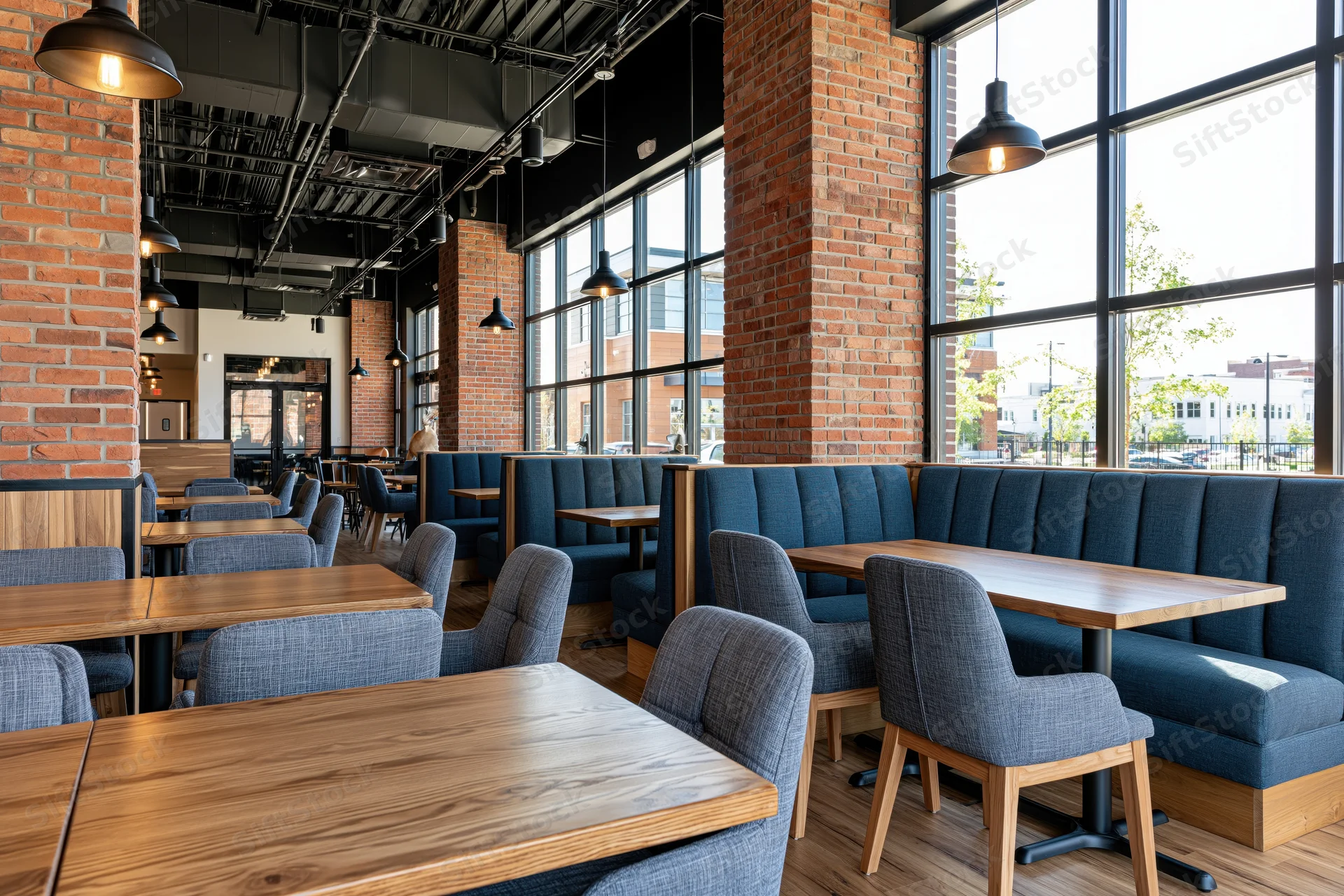 Modern restaurant interior with wooden tables and blue upholstered booths by large windows