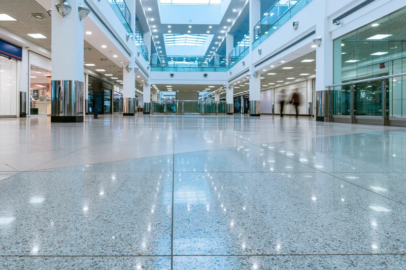 Wide view of empty modern shopping mall atrium with polished tile floor and glass railings