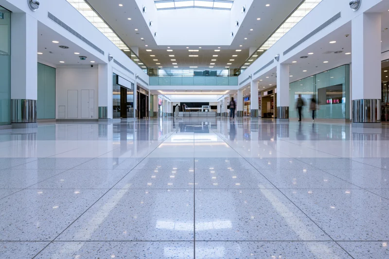 Wide view of empty modern shopping mall atrium with reflective tiled floor and glass walls