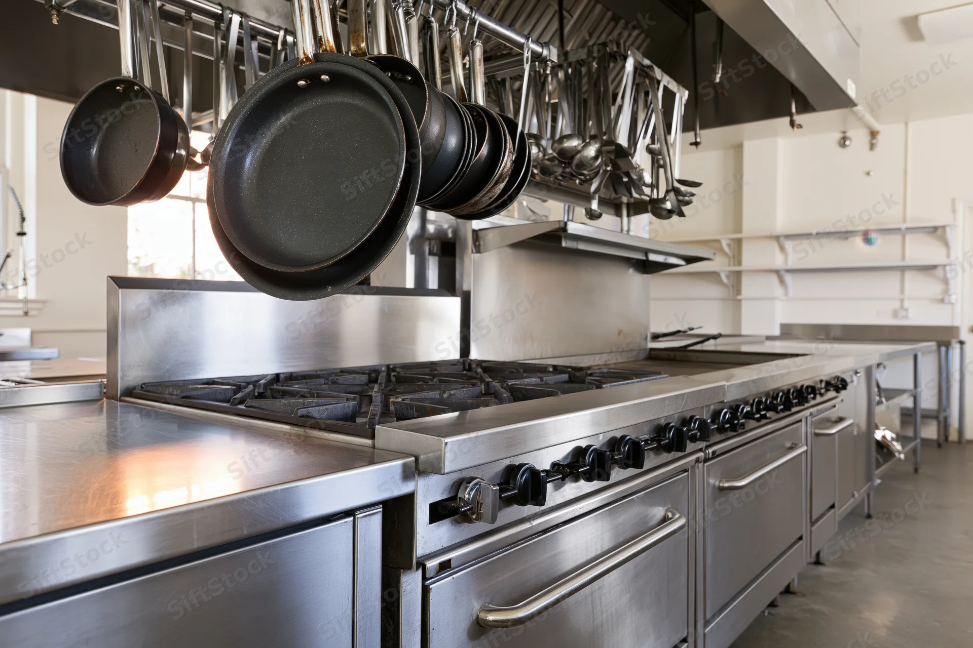 Stainless steel commercial kitchen with gas range and hanging cookware