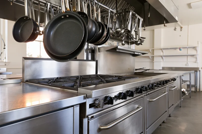 Stainless steel commercial kitchen with gas range and hanging cookware