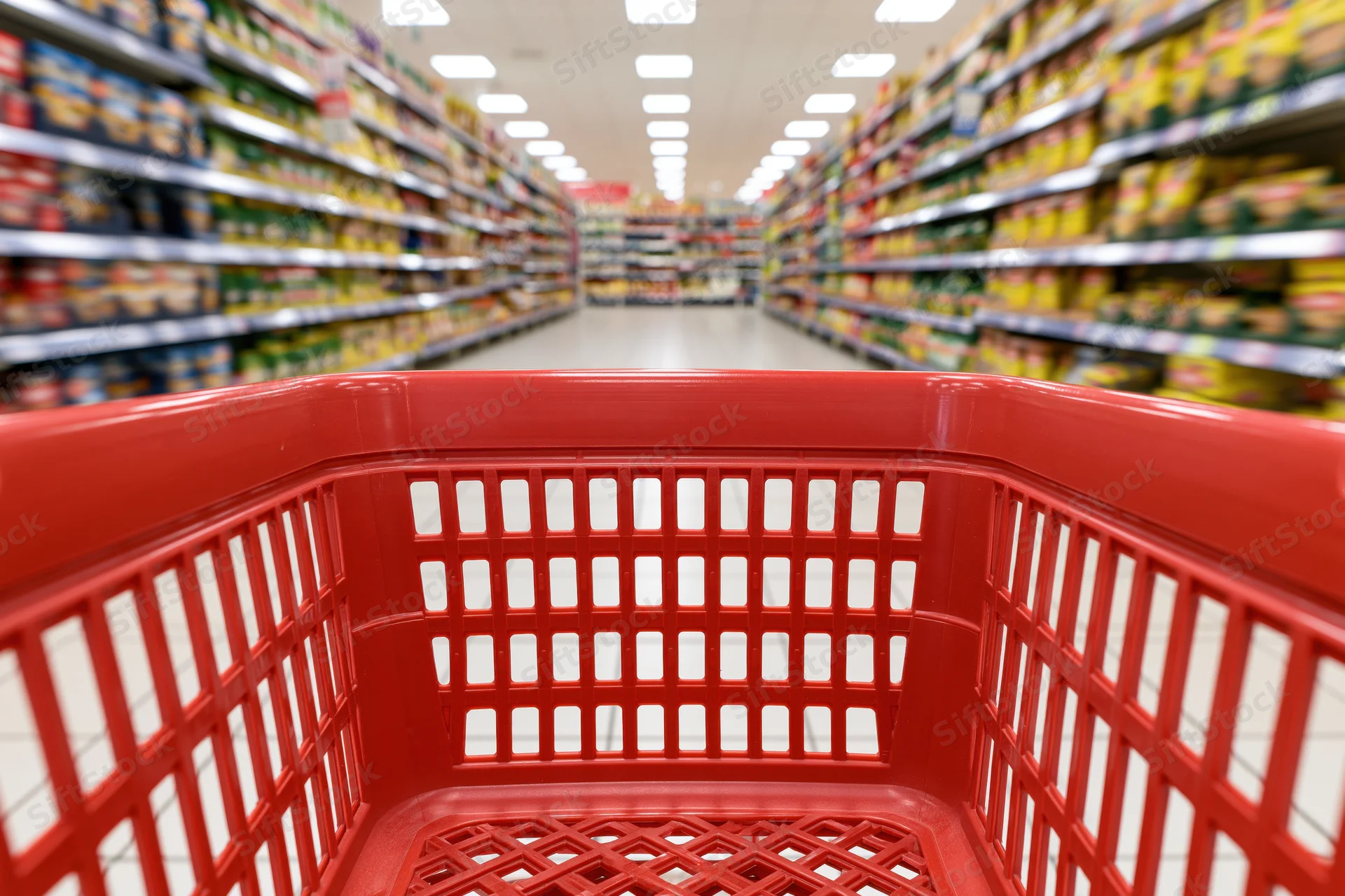 Empty red plastic shopping basket viewed from inside looking down supermarket aisle