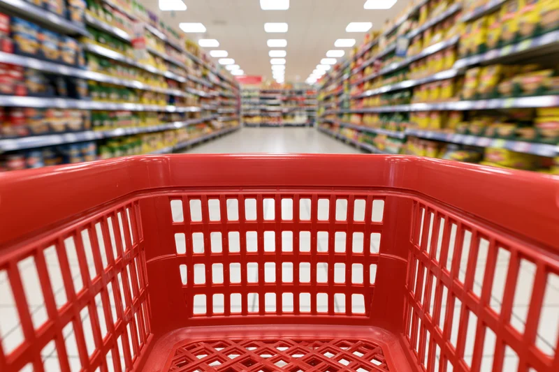 Empty red plastic shopping basket viewed from inside looking down supermarket aisle