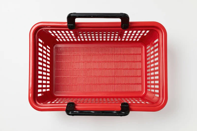 Empty red plastic shopping basket with black handles on white background