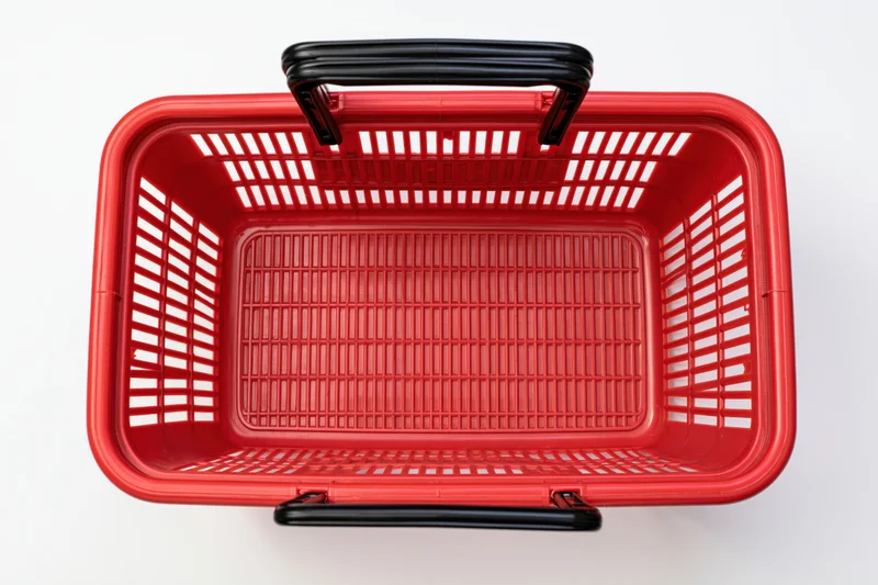 Empty red plastic shopping basket with black handles on white background