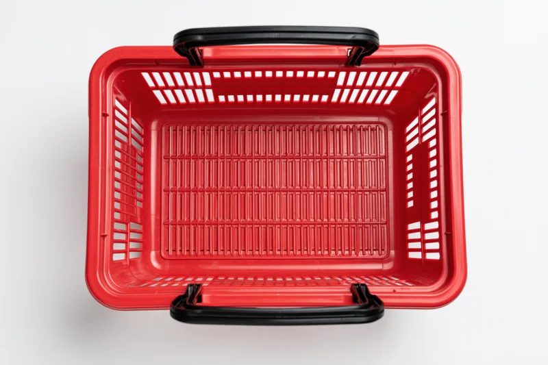 Empty red plastic shopping basket with black handles on white background