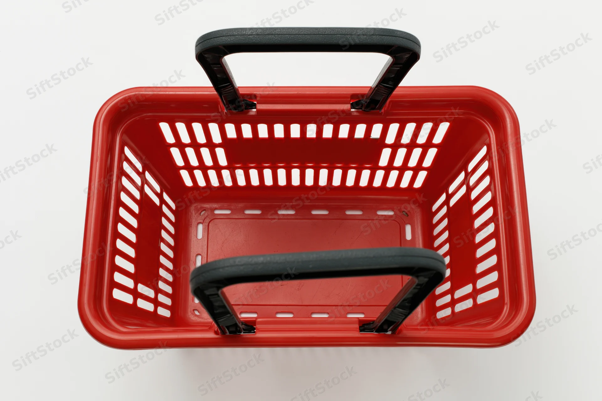 Empty red plastic shopping basket with black handles viewed from above on white background