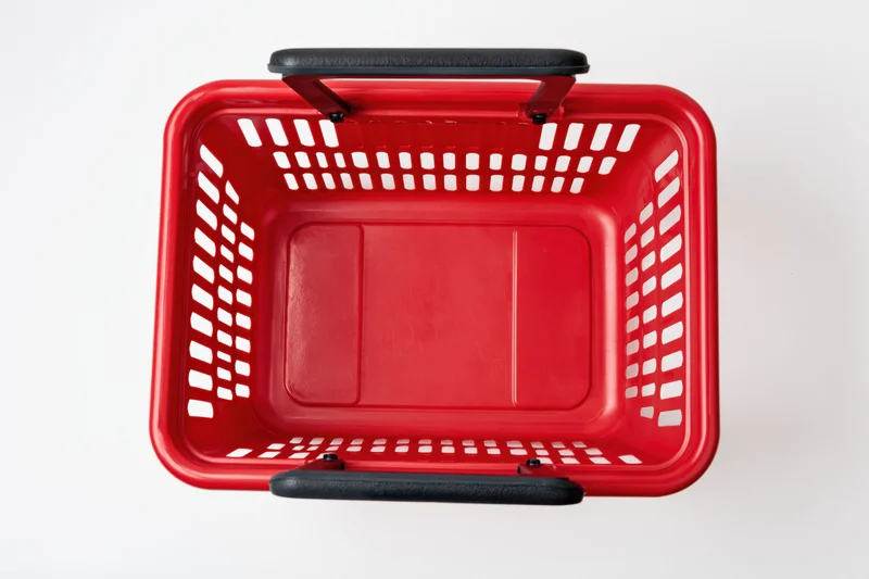 Empty red plastic shopping basket with black handles on white background