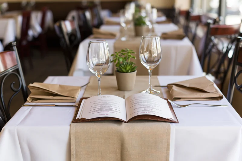 Open leather menu on a set restaurant table with wine glasses and napkins