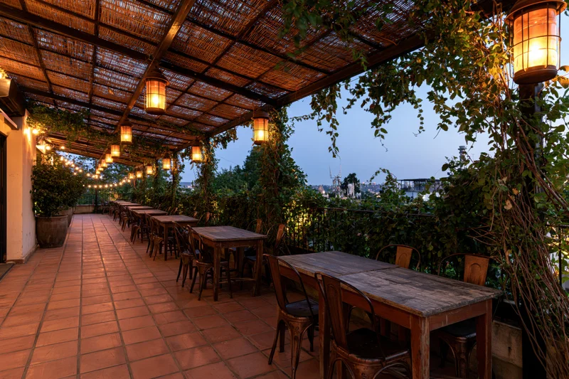 Empty rooftop restaurant terrace with wooden tables and chairs under a thatched roof at dusk