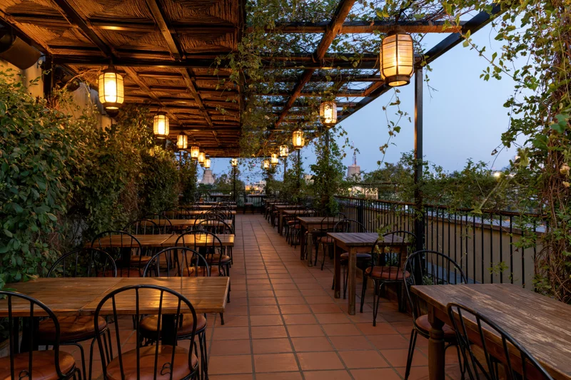 Empty rooftop restaurant terrace with wooden tables and hanging lanterns at dusk