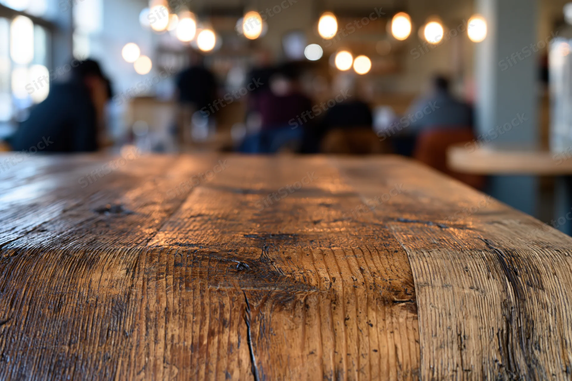 Rustic wooden table surface in sharp focus with blurred restaurant interior and warm lighting in background