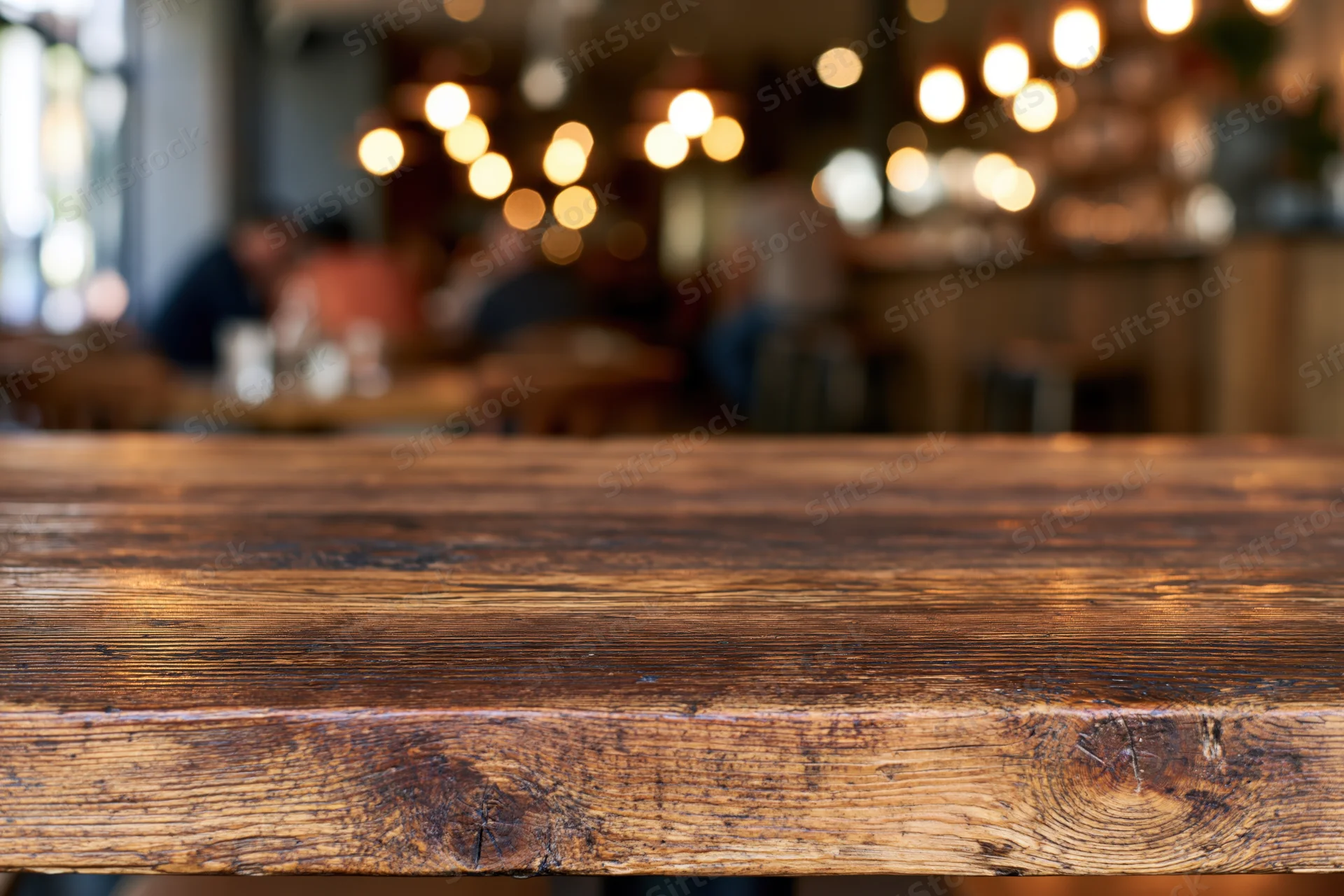 Rustic wooden table surface in sharp focus with blurred restaurant interior and warm lighting in background