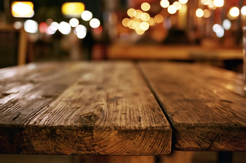Rustic wooden table surface in a dimly lit restaurant at night with blurred lights in the background