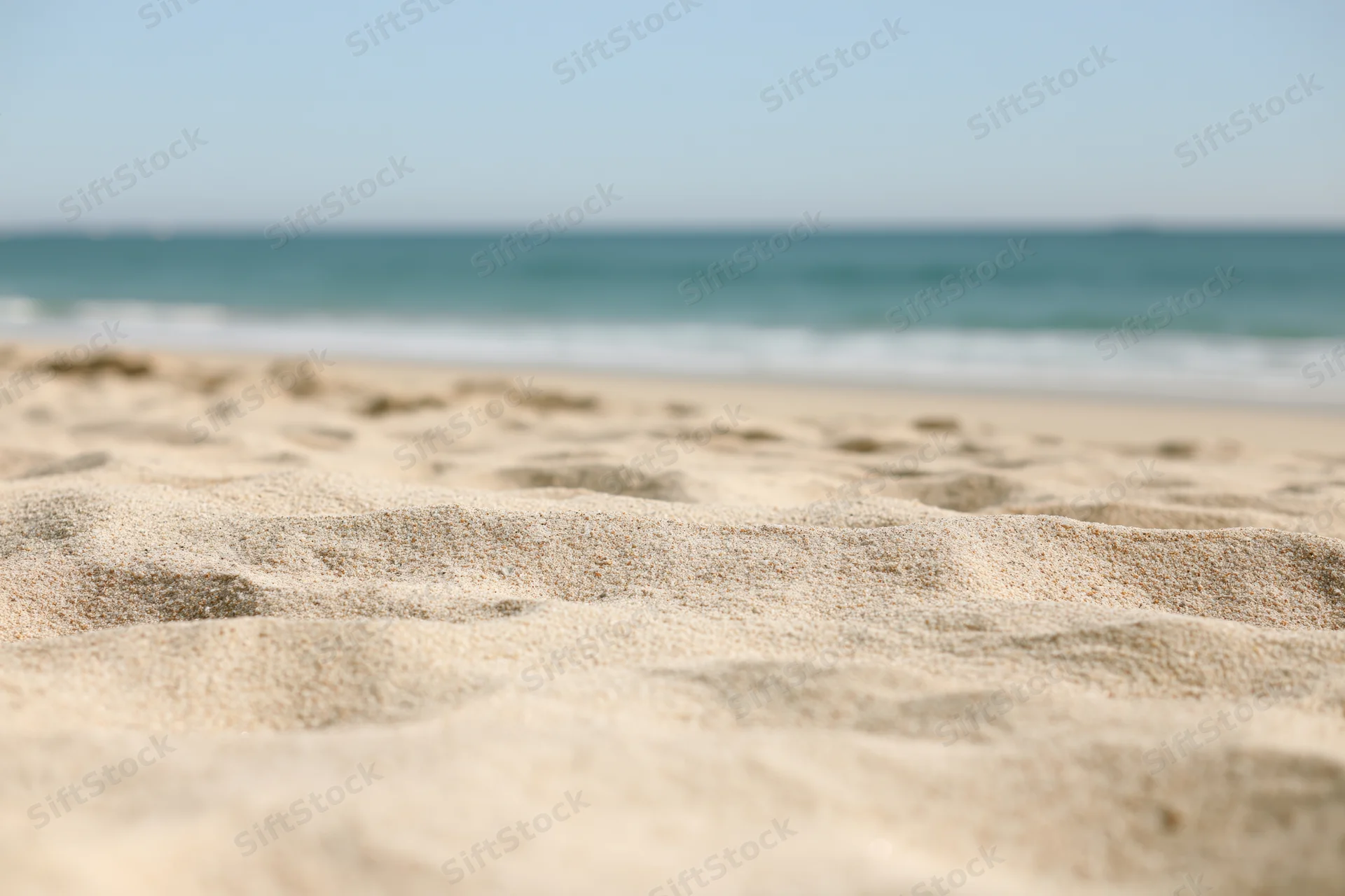 Close-up of textured sand on a beach with ocean waves in the background