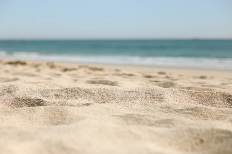 Close-up of textured sand on a beach with ocean waves in the background