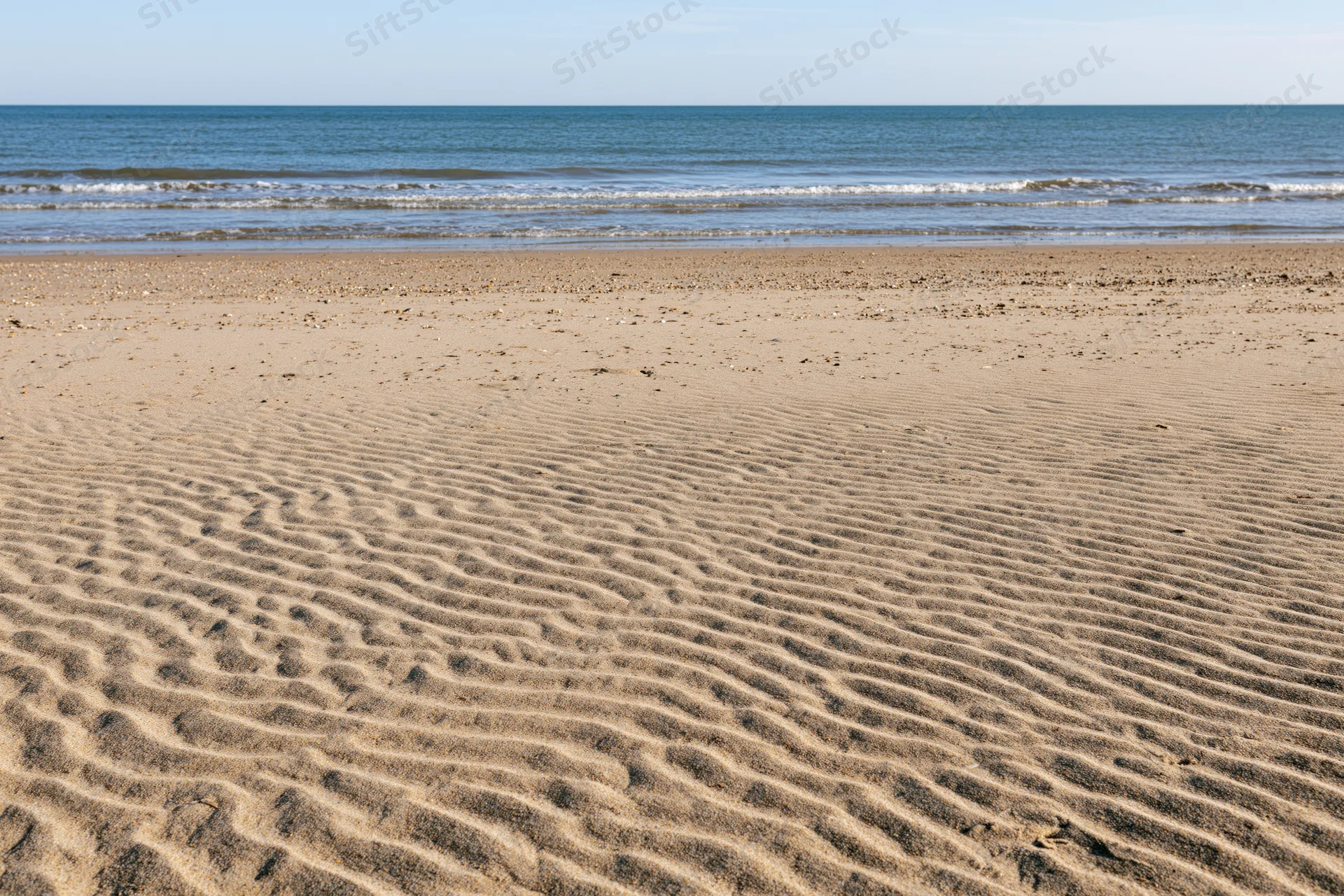 Rippled sand on a wide empty beach stretching toward calm ocean under clear sky