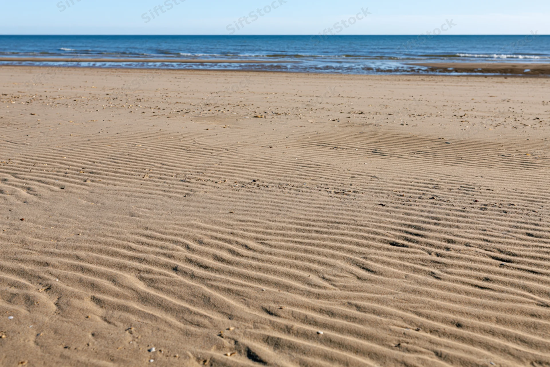 Sandy beach with rippled patterns stretching toward calm ocean under clear sky
