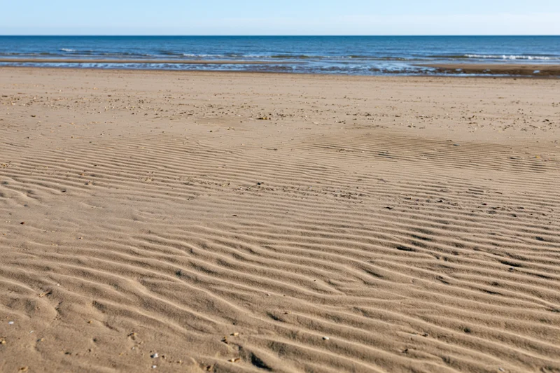 Sandy beach with rippled patterns stretching toward calm ocean under clear sky