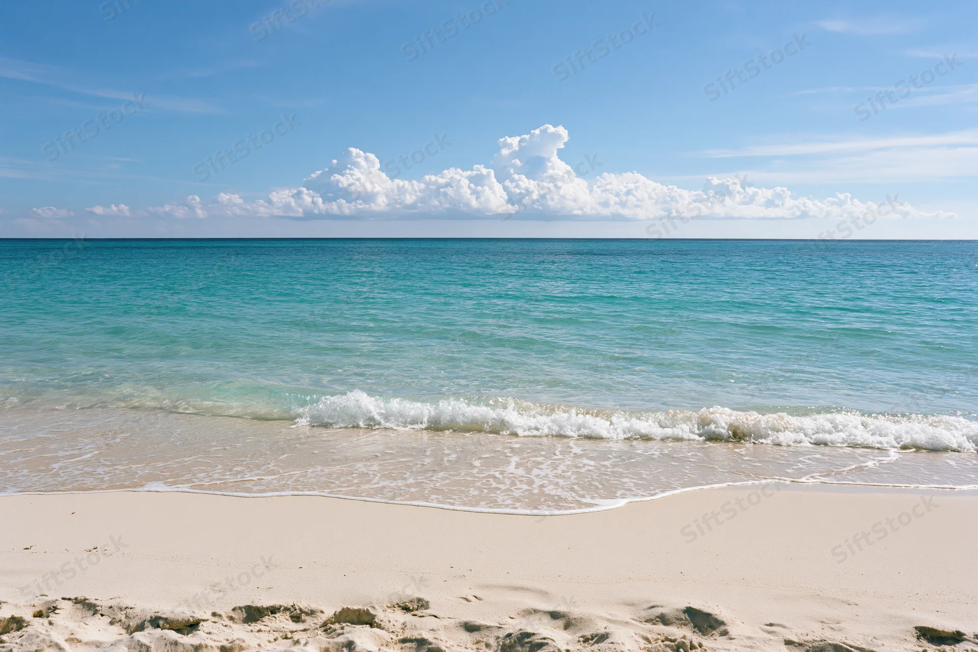 Gentle waves washing onto white sand at a tropical beach under a blue sky with clouds