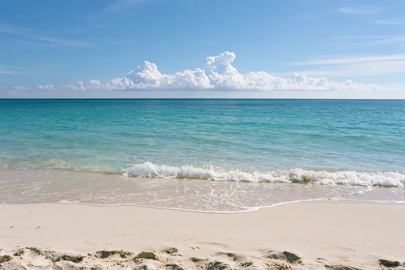 Gentle waves washing onto white sand at a tropical beach under a blue sky with clouds