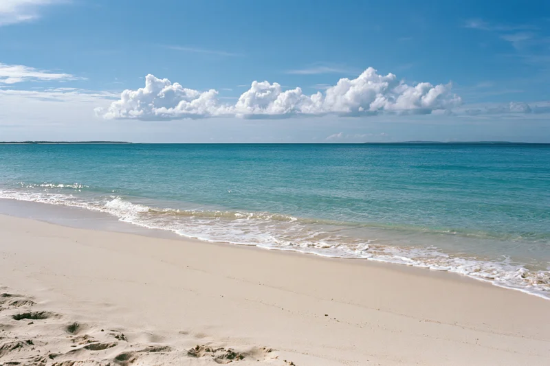 Gentle waves washing onto white sand at tropical beach under blue sky with clouds