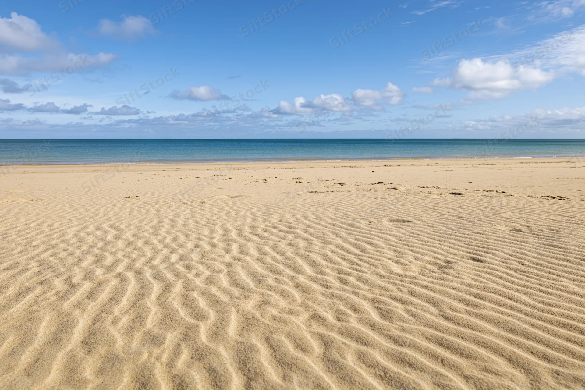 Rippled golden sand on a tropical beach under a blue sky with scattered clouds