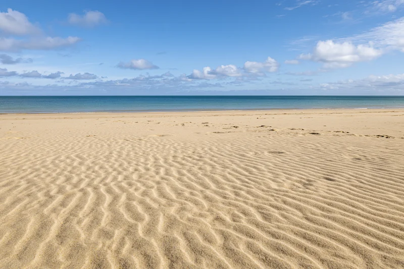 Rippled golden sand on a tropical beach under a blue sky with scattered clouds