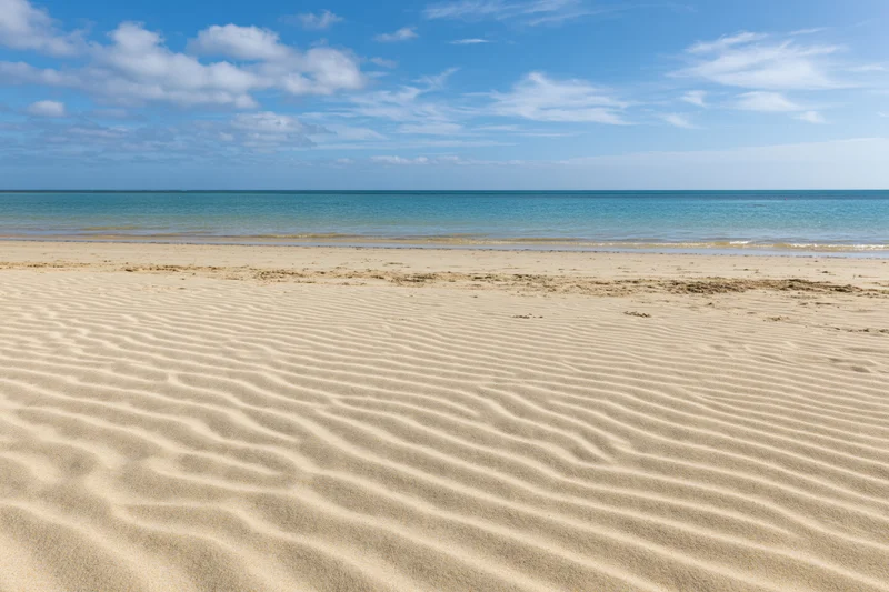 Rippled golden sand on a tropical beach under a blue sky with scattered clouds