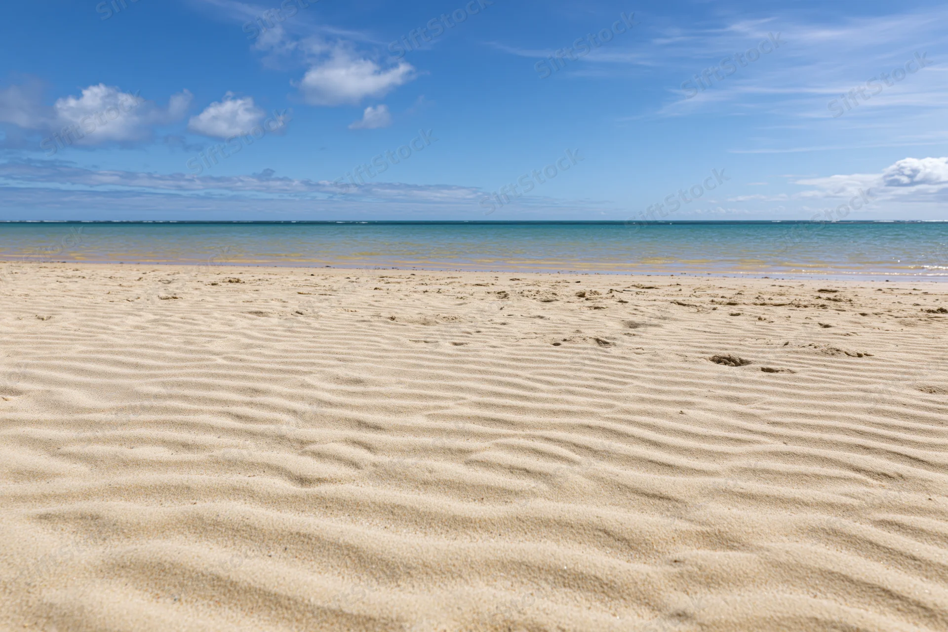 Rippled golden sand on a tropical beach under a clear blue sky with scattered clouds